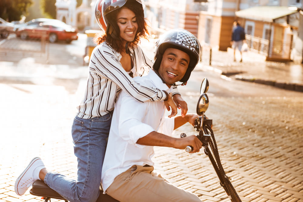 A couple riding a scooter through the city on a sunny day